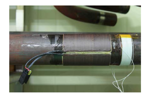 A phot shows two magnetic bands bonded to 2.5 inch pipe for DC bias (left) and manually wound coil for AC magnetization (right).