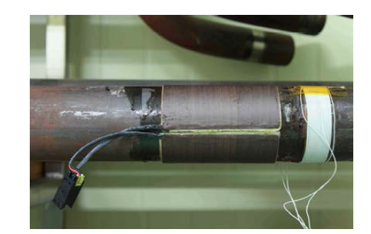 A phot shows two magnetic bands bonded to 2.5 inch pipe for DC bias (left) and manually wound coil for AC magnetization (right).